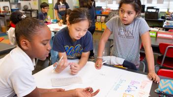 3 elementary students writing on flip chart in social studies unit